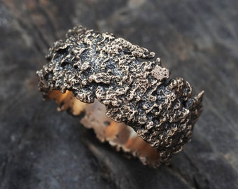 May include: A wide, textured bronze ring with a rough, organic surface. The ring is made of metal and has a dark brown color.