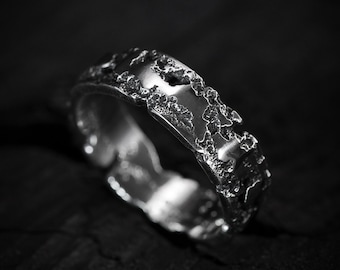 May include: A silver ring with a textured, irregular surface. The ring is thick and has a wide band.