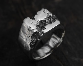 May include: A silver ring with a textured, rectangular band. The band has a rough, uneven surface.