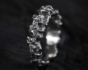 May include: A silver ring with a textured, organic design. The ring is made of a rough, uneven material, giving it a unique and modern look.