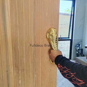 May include: A gold-coloured door handle shaped like an elephant's head. The handle is mounted on a wooden door. The text "Fulldeco Brass" is visible on the door.