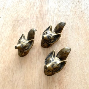 Könnte beinhalten: Drei goldfarbene Metall-Schubladengriffe in Form eines Fuchs-Kopfes. Jeder Griff zeigt einen detaillierten Fuchs-Kopf mit einem eingerollten Schwanz.