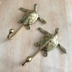 May include: Two brass turtle hooks with a gold finish. Each hook is shaped like a turtle with a curved hook extending from the turtle's body.