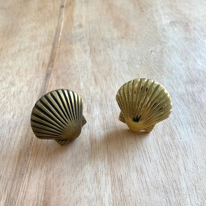 Op de afbeelding: Twee gouden trekknoppen in de vorm van een schelp. De knoppen zijn gemaakt van metaal en hebben een gedetailleerd, getextureerd oppervlak.