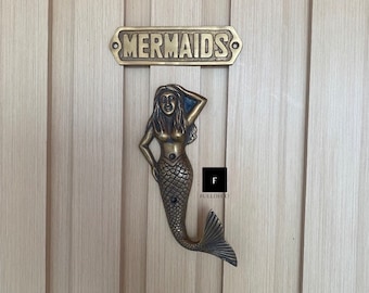 May include: A brass mermaid door knocker with a sign that reads "MERMAIDS" above it.