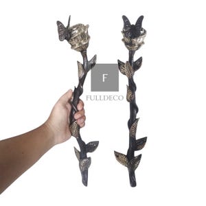 May include: Two ornate metal door handles shaped like roses with butterflies on top. The handles are black with gold accents and have a detailed design.