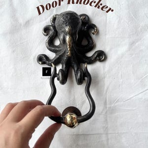 Op de afbeelding: Bronzen octopus deurbel met de tekst "Door Knocker" in bruin. De klopper heeft een gedetailleerd octopusontwerp met een donkere bronzen afwerking en een goudkleurige handgreep.