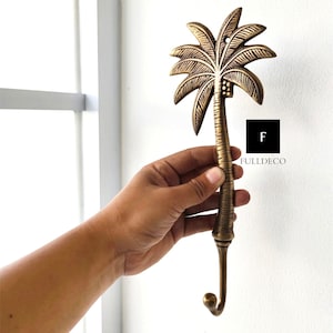 May include: A gold palm tree shaped wall hook. The hook is made of metal and has a detailed design. The hook is perfect for hanging towels, coats, or other items.
