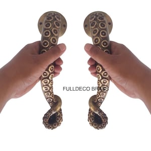May include: A pair of antique brass door handles shaped like octopus tentacles. The handles are detailed with textured circles and have a knotted design at the bottom.