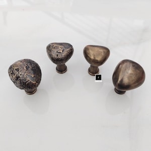 Może przedstawiać: Cztery antyczne brązowe gałki do szafek z fakturowanym, kamiennym wykończeniem. Gałki mają kształt zaokrąglonego owalu.