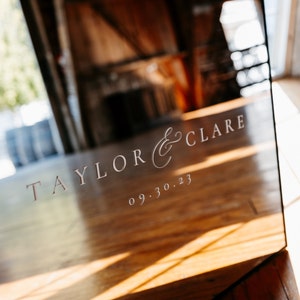 May include: A mirrored sign with the text "TAYLOR & CLARE" and the date "09.30.23" in a light pink font.