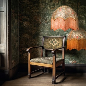 May include: A wooden armchair with a patterned fabric seat and back sits in a room with patterned wallpaper and two lampshades with fringe. The lampshades are covered in a floral pattern.