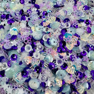May include: A mix of iridescent blue, purple, and white sequins and beads in various shapes, including stars, shells, and circles.