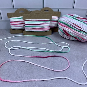 May include: Three spools of white, pink, and green striped cotton rope with a ball of the same rope. The rope is on a white tiled surface.
