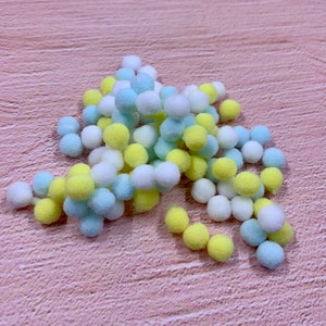 May include: A pile of small, fluffy pom-poms in yellow, white, and light blue colors.