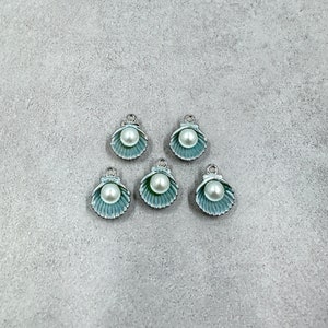 May include: Five silver charm pendants shaped like seashells with a white pearl in the center of each.