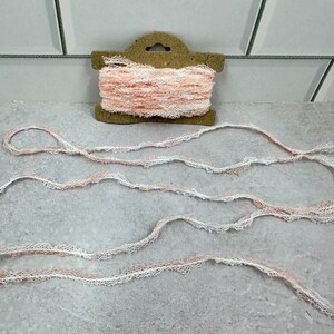 May include: A spool of white and peach lace trim. The lace is delicate and has a scalloped edge.