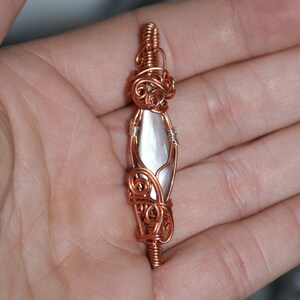 May include: A copper wire wrapped pendant featuring a pearlescent iridescent stone. The pendant is a unique and delicate piece of jewelry.