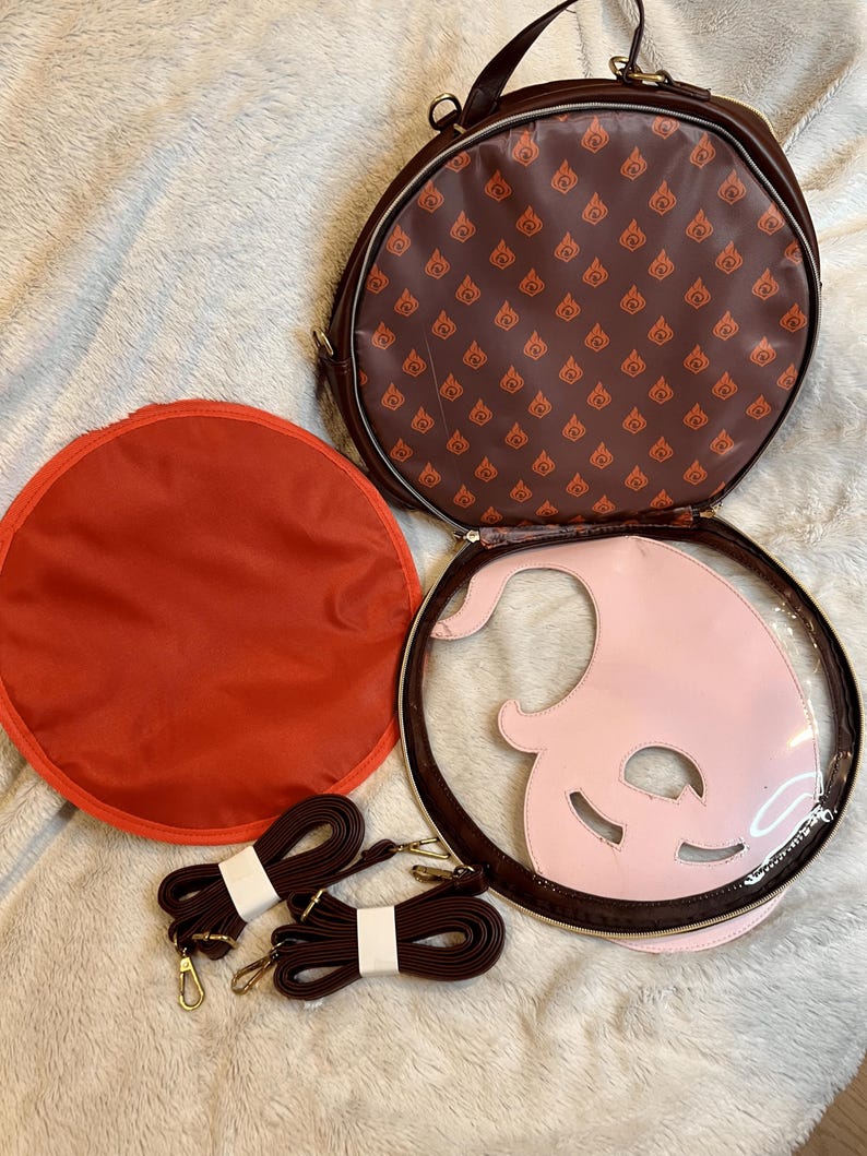 May include: A brown round bag with a pink and clear plastic insert. The bag has a brown strap and a red lining. The bag has a repeating pattern of a flame design on the outside.
