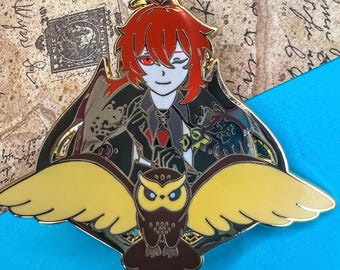 May include: A gold-toned enamel pin featuring a character with red hair and a black outfit, holding a golden owl with outstretched wings. The character has a winking expression and is wearing a red tie. The pin has a detailed design with a black and gold background.