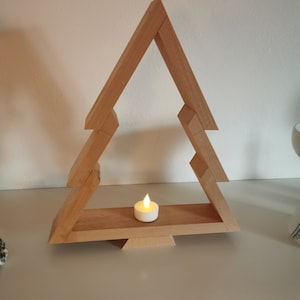 May include: A wooden Christmas tree shaped candle holder with a small white candle inside. The candle is lit and glowing.