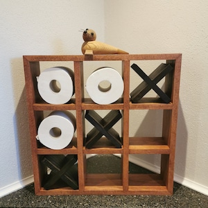 以下が含まれることがあります： 9つの区画があり、各区画にトイレットペーパーのロールまたは木製のXまたはOが入っている木製の三目並べゲーム。木製のあざらしの置物がゲームの上に置かれています。