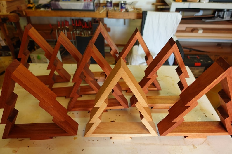 May include: A set of eight wooden Christmas tree-shaped shelves, some stained a darker brown and others a lighter natural wood color. The shelves are arranged in a staggered pattern on a light wood surface.
