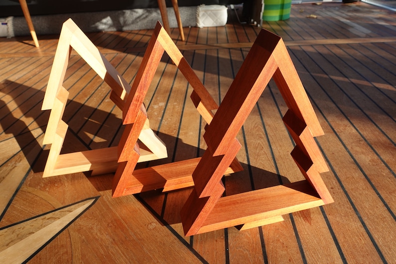 May include: Three wooden Christmas tree ornaments in different shades of brown. The ornaments are made of wood and have a simple, geometric design.