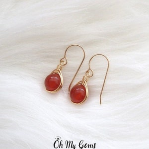May include: A pair of gold wire wrapped carnelian earrings. The earrings are teardrop shaped and have a red carnelian stone in the center.