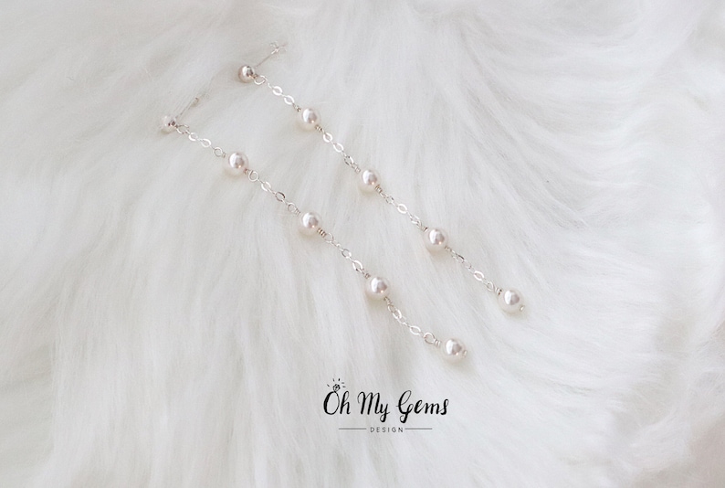 Puede incluir: Elegantes pendientes de plata con perlas colgantes. Cada pendiente presenta una delicada cadena con m&uacute;ltiples perlas, creando un dise&ntilde;o elegante y fluido. Los pendientes se colocan sobre un fondo blanco suave.