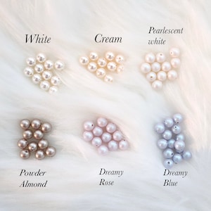 Puede incluir: Un conjunto de perlas en varios colores, incluyendo blanco, crema, blanco nacarado, almendra en polvo, rosa so&ntilde;ador y azul so&ntilde;ador. Cada color est&aacute; etiquetado con una escritura elegante sobre un fondo blanco y esponjoso.