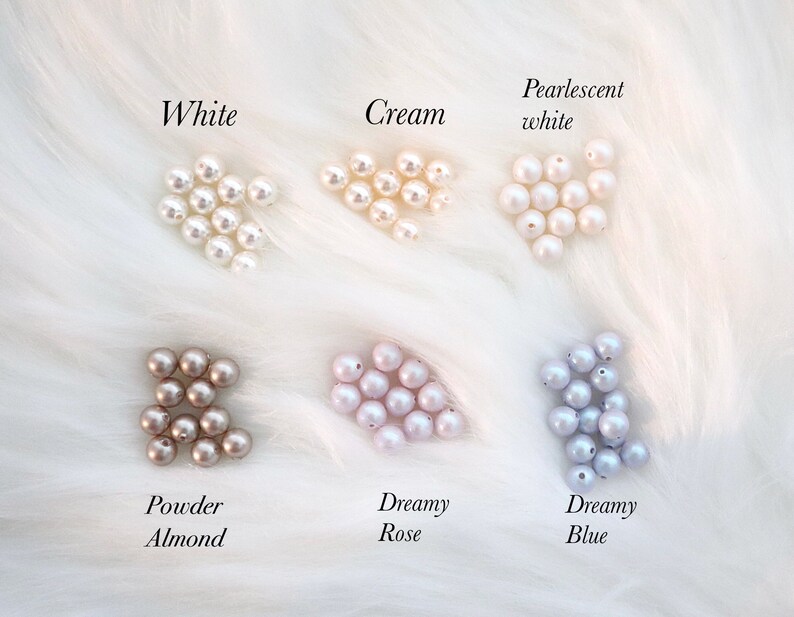 Puede incluir: Un conjunto de perlas en varios colores, incluyendo blanco, crema, blanco nacarado, almendra en polvo, rosa so&ntilde;ador y azul so&ntilde;ador. Cada color est&aacute; etiquetado con una escritura elegante sobre un fondo blanco y esponjoso.