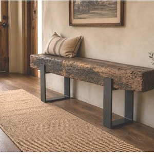 May include: A bench featuring a thick, rectangular, reclaimed wood seat with a rough, weathered texture, supported by two black, U-shaped metal legs. A rectangular throw pillow with a striped pattern rests on the wooden surface.