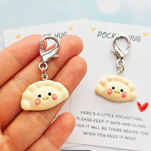 May include: A pair of pocket hug charms. Each charm features a smiling dumpling design with rosy cheeks, attached to a silver-colored clasp. The charms are displayed with a card that reads "Pocket Hug".