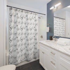 May include: A white shower curtain with a black and white abstract pattern of repeated figures. The shower curtain is hung in a white bathroom with a white vanity and a white toilet.