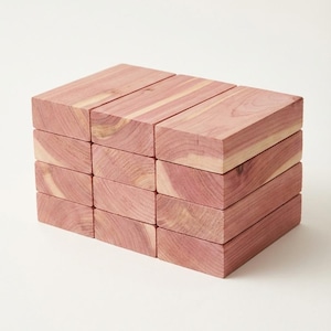 May include: A stack of twelve rectangular cedar wood blocks. The blocks are a reddish-pink color with visible wood grain. The blocks are arranged in three rows of four, creating a compact, organized presentation.