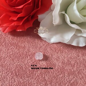 May include: A small, translucent silicone cushion pad, labeled "9.5 M SILICONE CUSHION PAD," rests on a textured pink surface. The background features red and white fabric flowers. The image includes the logo "A ONE JEWEL."
