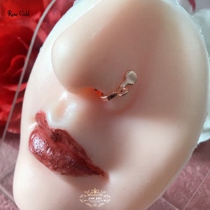 May include: Rose gold nose cuff jewelry. The jewelry is a clip-on style, featuring a small, rounded design. The text "Rose Gold" is visible in the upper left corner. The jewelry is displayed on a mannequin head.