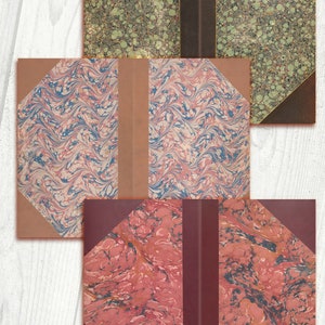 May include: Three book covers with marbled paper designs. The top cover is green and brown, the middle cover is pink and blue, and the bottom cover is red and black.