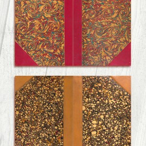 May include: Two antique book covers with marbled paper designs. The top cover has a red spine and a swirling pattern in shades of red, yellow, and blue. The bottom cover has a brown spine and a pattern of small, round spots in shades of brown, yellow, and red.