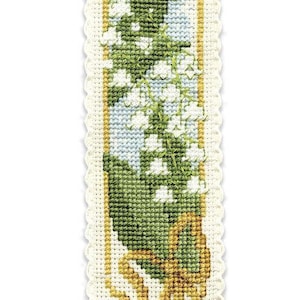 May include: Cross-stitched bookmark featuring a floral design of white lily of the valley flowers with green leaves and stems. The bookmark has a light blue tassel and a scalloped edge.