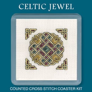 May include: A counted cross stitch coaster kit with a Celtic knot design. The coaster features a central knot pattern in gold, burgundy, and green, with smaller corner designs. The text "CELTIC JEWEL" and "COUNTED CROSS STITCH COASTER KIT" are visible.