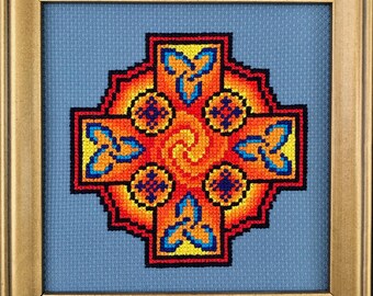 Puede incluir: Un mandala en forma de cruz con un esquema de colores azul, naranja y amarillo. El mandala está enmarcado en un marco dorado.