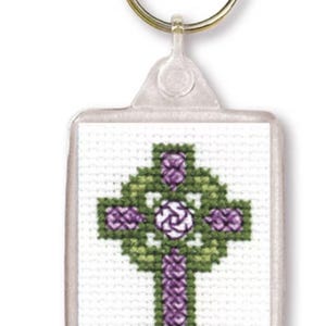 May include: A clear plastic keychain with a cross-stitch design. The design features a Celtic cross in shades of green and purple, with a white center. The keychain has a metal ring for attaching keys.