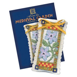 May include: Two lavender sachets with cross-stitched floral designs, featuring blue and purple flowers with green stems, are displayed in front of a blue book. The sachets have a yellow ribbon and a decorative border. The book reads "From the Medieval Garden".