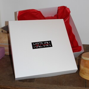 May include: White gift box with a red tissue paper lining. The box has a black label with the text "KAZVAN" in white letters and "hats & accessories" in red letters.