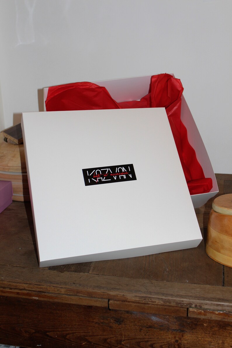 May include: White gift box with a red tissue paper lining. The box has a black label with the text "KAZVAN" in white letters and "hats & accessories" in red letters.