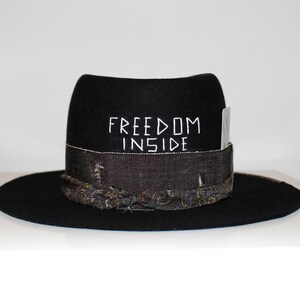 May include: Black felt fedora hat with a patterned band and the words "FREEDOM INSIDE" embroidered on the crown.