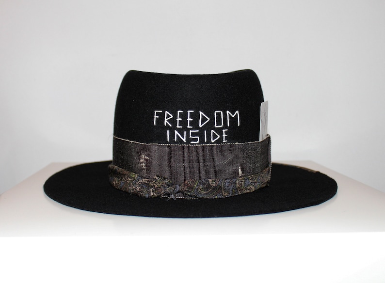 May include: Black felt fedora hat with a patterned band and the words "FREEDOM INSIDE" embroidered on the crown.