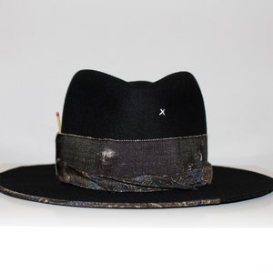 May include: A black felt fedora hat with a wide brim and a patterned band. The hat has a small white 'x' on the crown.